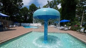 Ein Swimmingpool mit einer Wassersäule, umgeben von Liegestühlen und Sonnenschirmen.