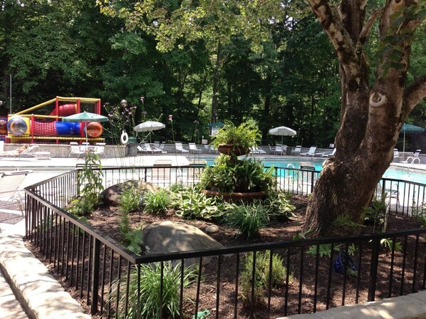 A pool area with a fenced garden, lounge chairs, and a children's play structure in the background.