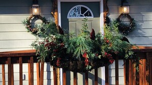Ein Haus mit einer Holzterrasse, einer weißen Tür und zwei Wandleuchten.