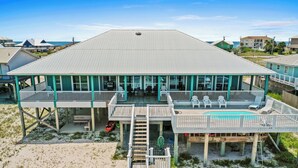 Et hus ved stranden med en overdækket veranda, en pool og en trappe op til øvre plan.