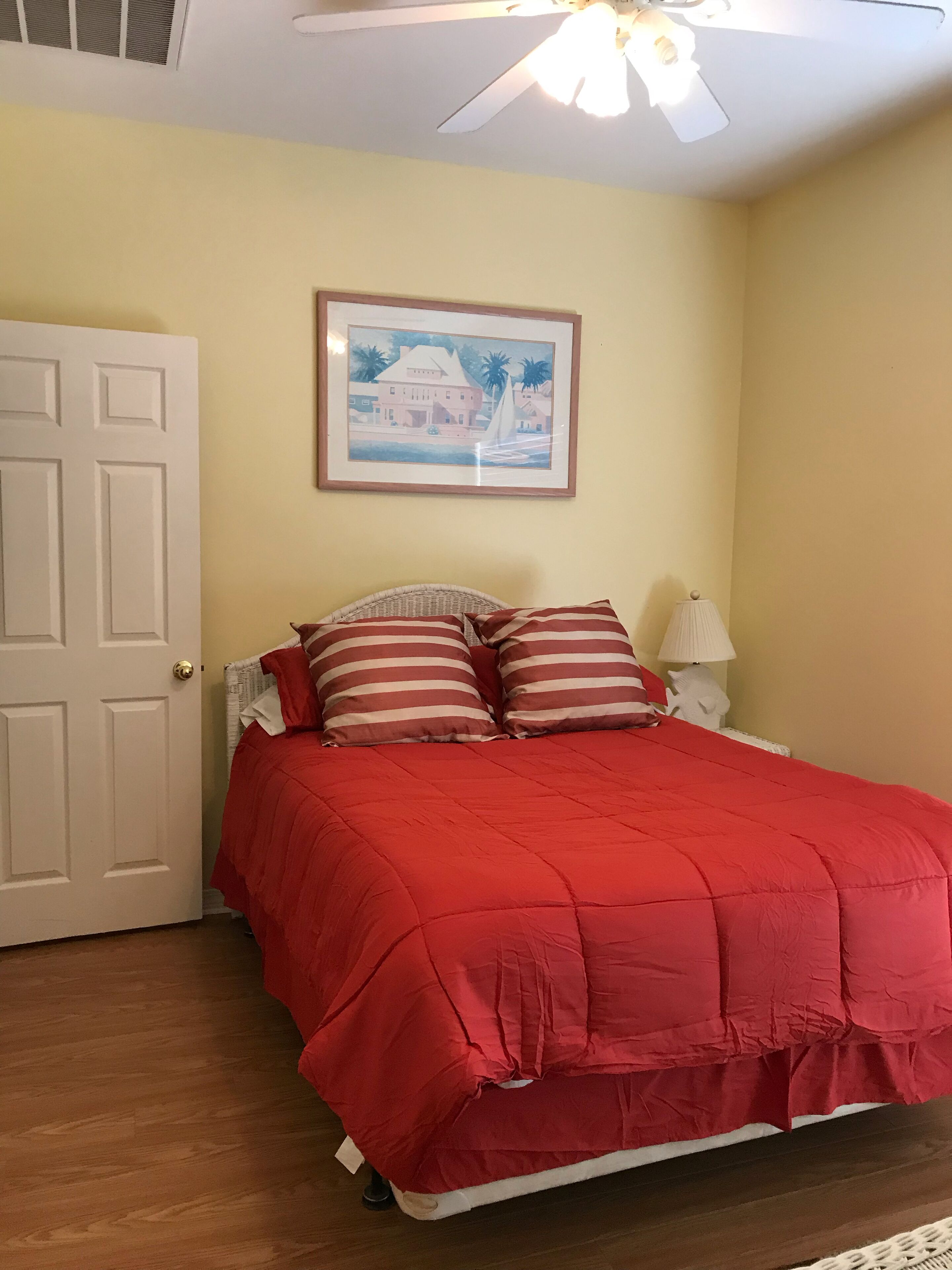 Un dormitorio con cama, una puerta, un cuadro en la pared y un ventilador de techo.