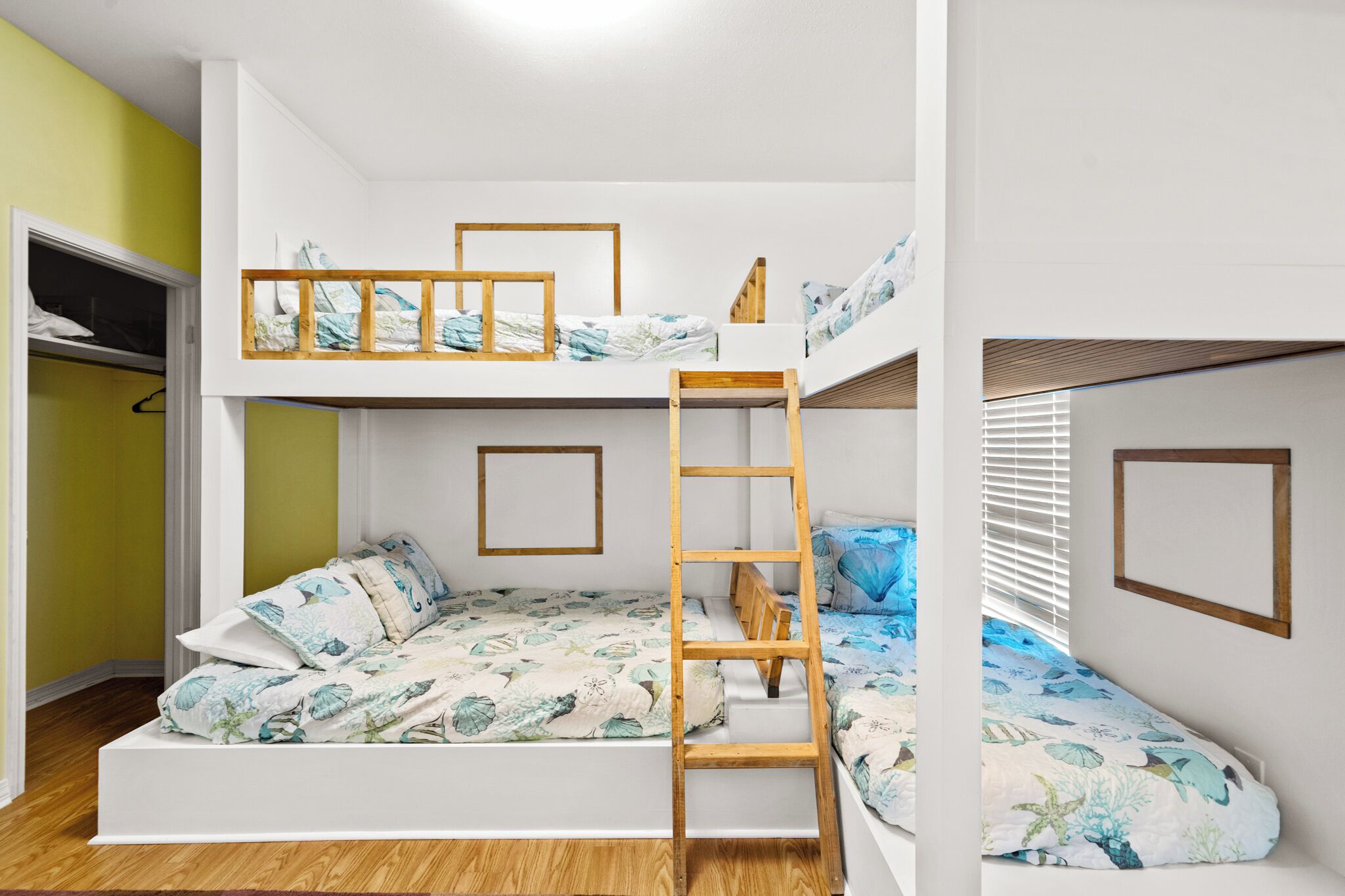 A bunk bed room with a ladder, a wardrobe, and a window with blinds.