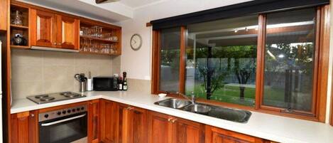 A kitchen with wooden cabinets, a microwave, stove, and a large window with a view of greenery.