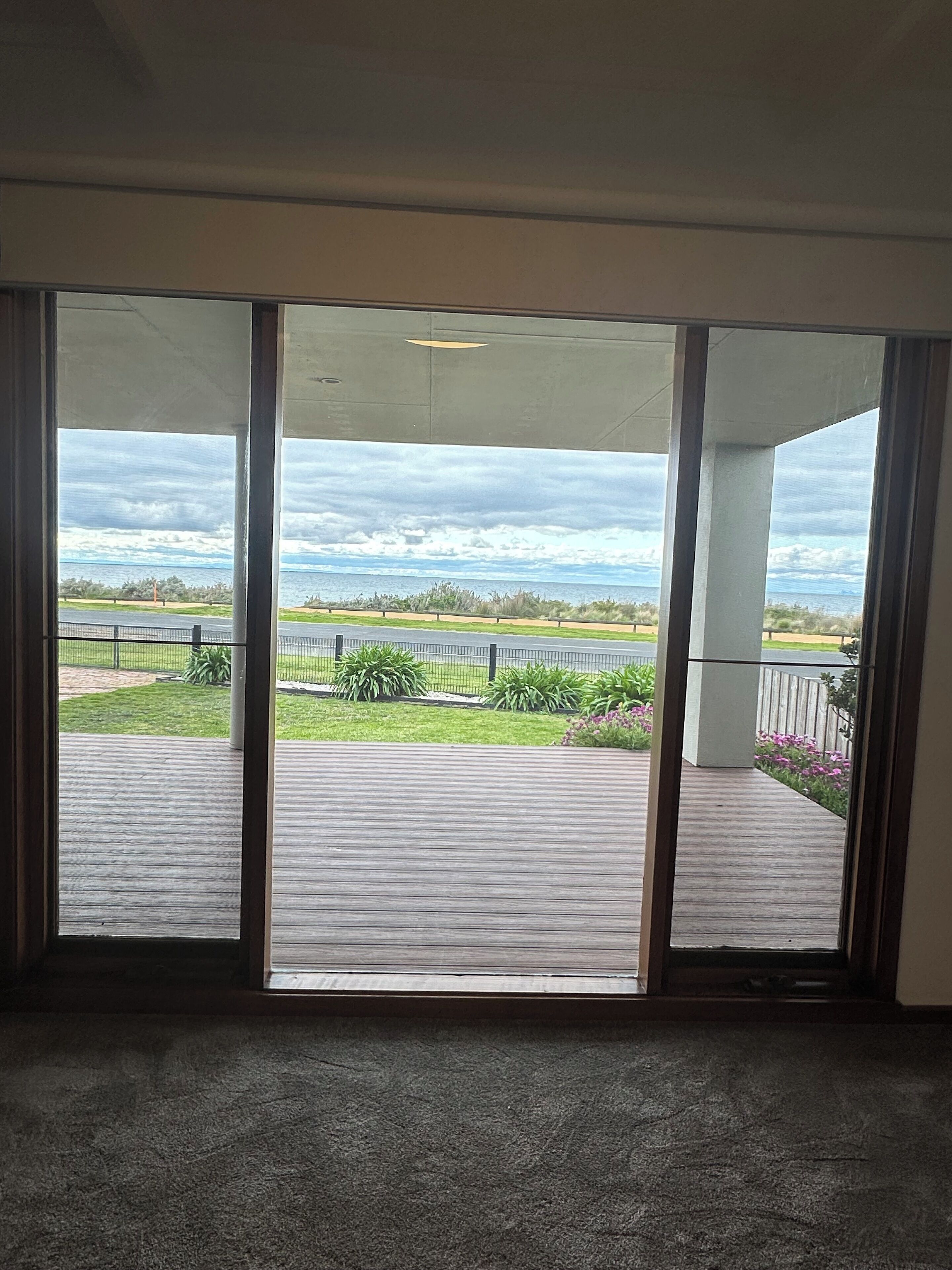 Et værelse med en stor skydedør, der fører ud til en terrasse med udsigt over en strand og et hav.