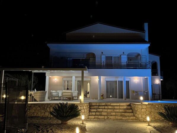 A two-story house with a balcony, a patio area with seating, and a stone wall.