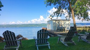 A lakeside view with Adirondack chairs, a dock, and a small cabin. - Cayuga Lake Cottage near Ithaca, Taughannock Falls State Park and Trumansburg, N (Trumansburg)