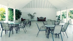 A spacious covered patio with tables and chairs, a sofa, and potted plants. - 24 gated security studio apartment,  Seawind on the bay Freeport Mobay (Montego Bay)