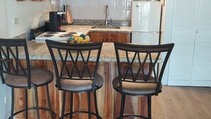 A compact kitchen with wooden cabinets, a granite countertop, a stainless steel refrigerator, and a central island with bar stools. - 24 gated security studio apartment,  Seawind on the bay Freeport Mobay (Montego Bay)