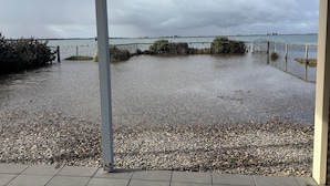 Zona per a vianants inundada amb una tanca metàl·lica i una vista d'un cos d'aigua al fons.