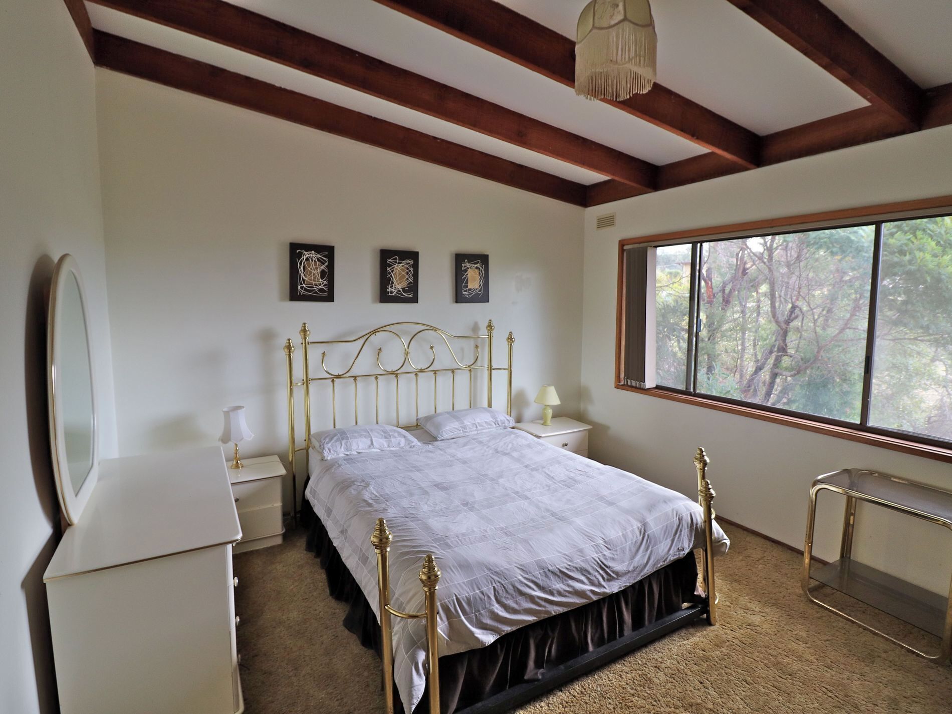 Une chambre à coucher avec un lit, des tables de chevet, un miroir et une fenêtre donnant sur des arbres.