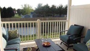 A balcony with a wooden table, two green armchairs, and a view of a residential area. - Spacious and Well Appointed Three Bedroom, Two Bath Condo situated just outside the Town of Lewes Delaware (Lewes)