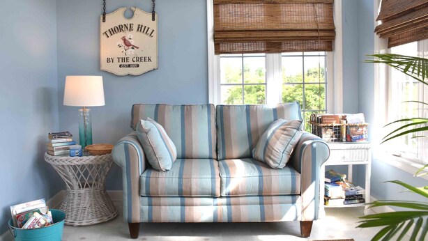 A cozy living room with a striped sofa, a wicker side table, a lamp, and a sign reading "Thorne Hill by the Creek." - Spacious and Well Appointed Three Bedroom, Two Bath Condo situated just outside the Town of Lewes Delaware (Lewes)