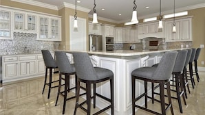 A spacious kitchen with white cabinetry, a large island with bar stools, and pendant lighting. - Luxurious Oceanfront Home: Pool, SPA, & Movie Theater (Murrells Inlet)
