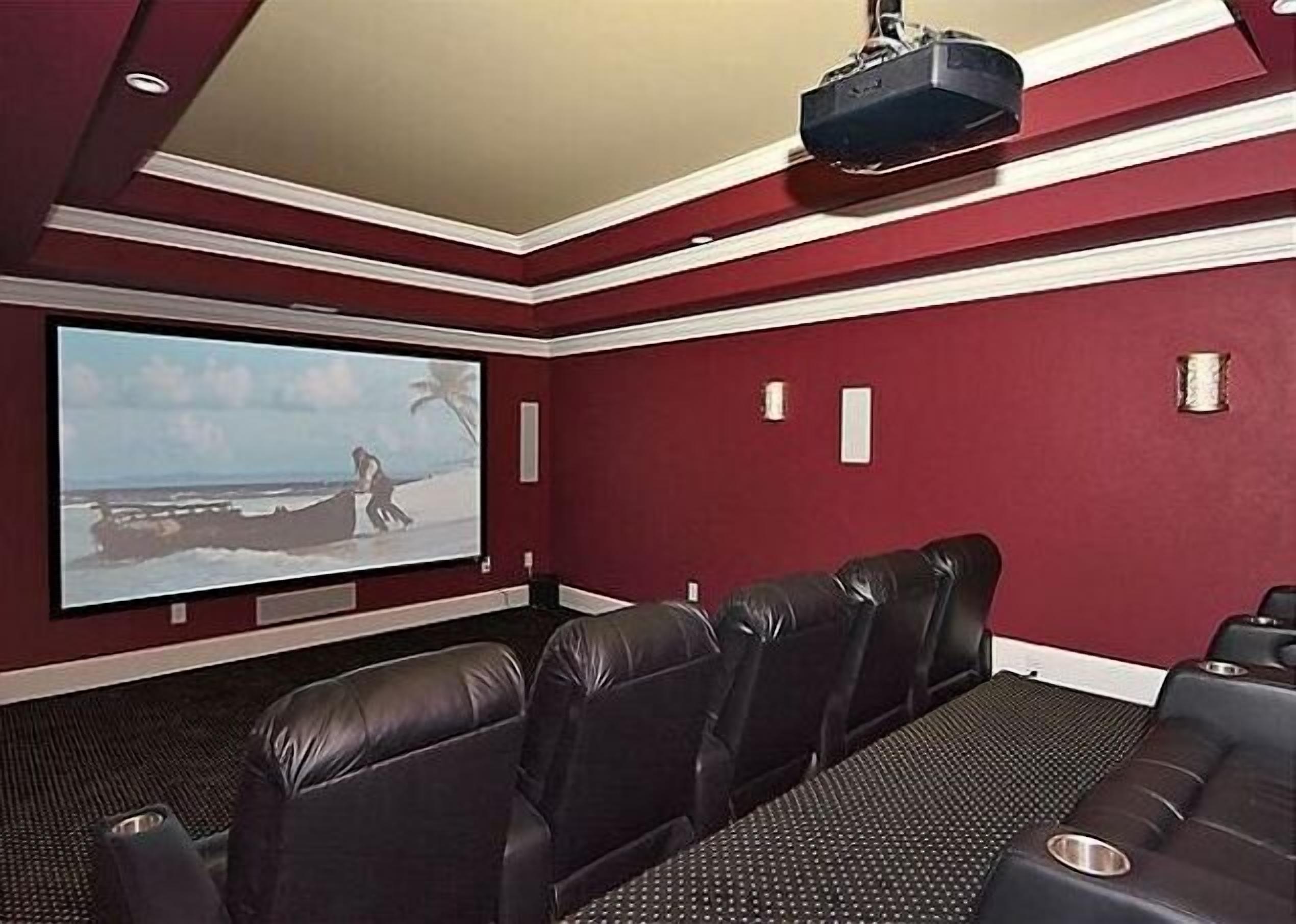 Un cine en casa con una pantalla grande, asientos de cuero y un proyector instalado en el techo.