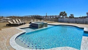 A swimming pool with lounge chairs and a hot tub, surrounded by a fence and palm trees. - Luxurious Oceanfront Home: Pool, SPA, & Movie Theater (Murrells Inlet)
