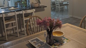 Uma área de refeições com uma mesa posta para dois, um vaso com flores e uma tigela sobre a mesa.