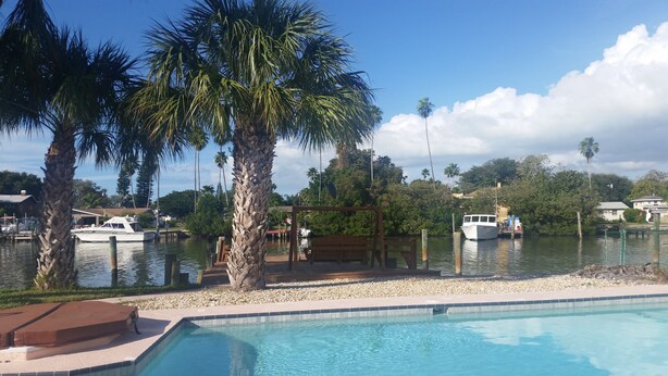Piscina com vista para um porto, palmeiras e barcos.