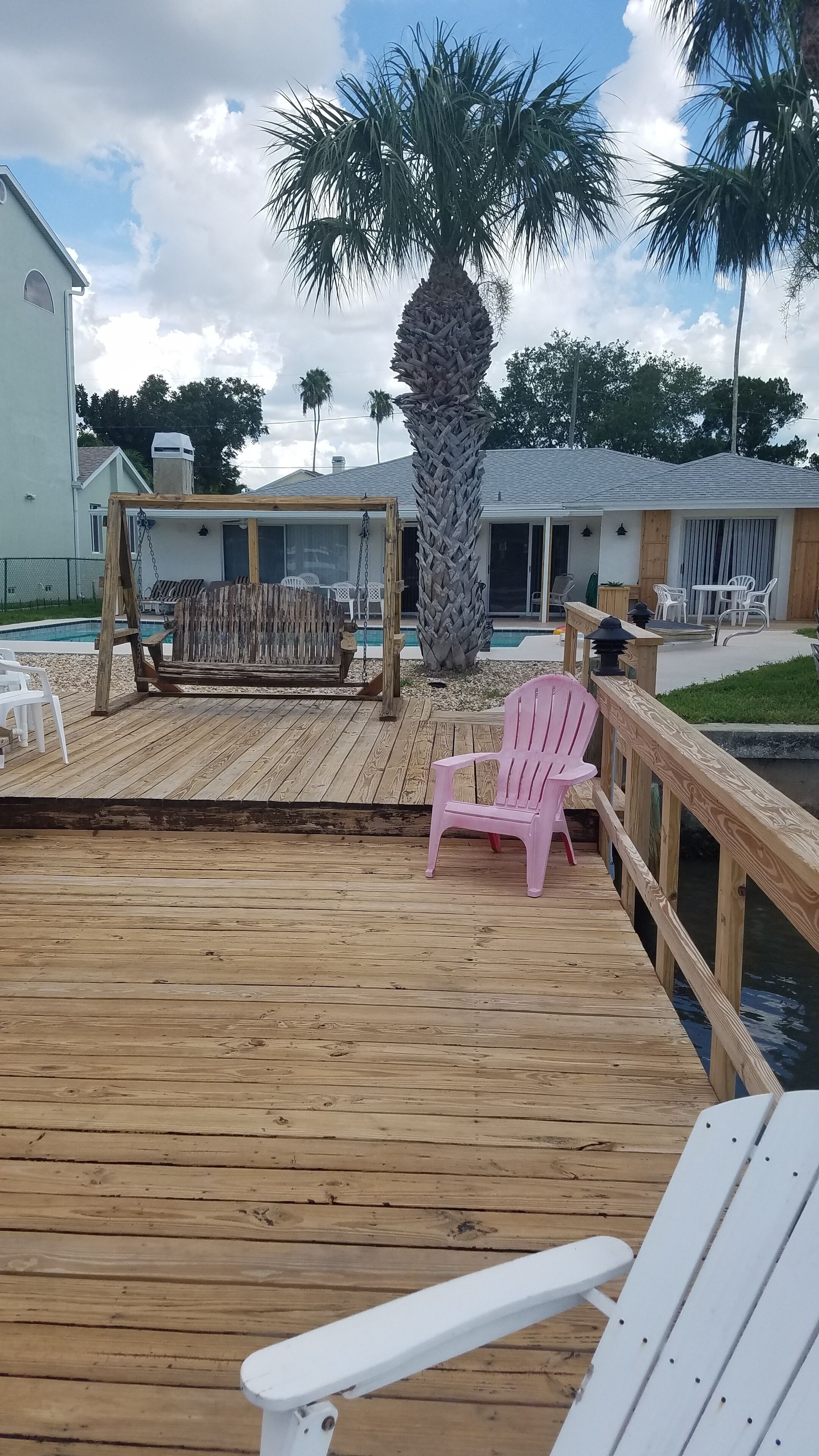 Eine Holzterrasse mit Pool, Palme und Gartenmöbeln.