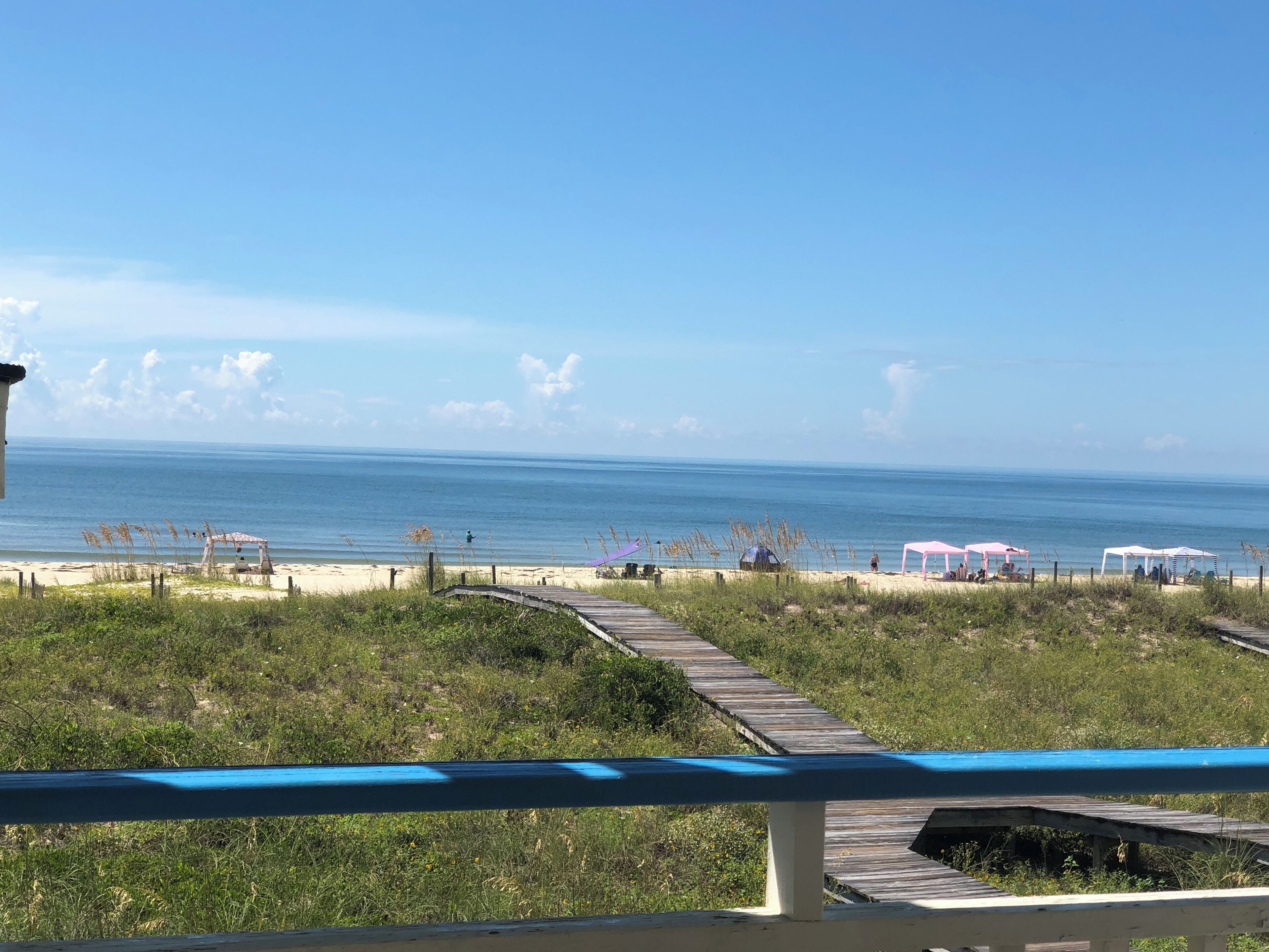 A beach with a wooden boardwalk leading to the shore, a sandy beach, and a clear blue sky.