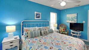 A bedroom with a bed, a TV, a ceiling fan, and a window.