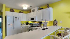 A kitchen with white cabinets, a microwave, stove, and a refrigerator. There are two wicker chairs and a decorative starfish.