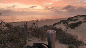 A beach scene with a sunset, a metal cup, and a pair of black sandals.