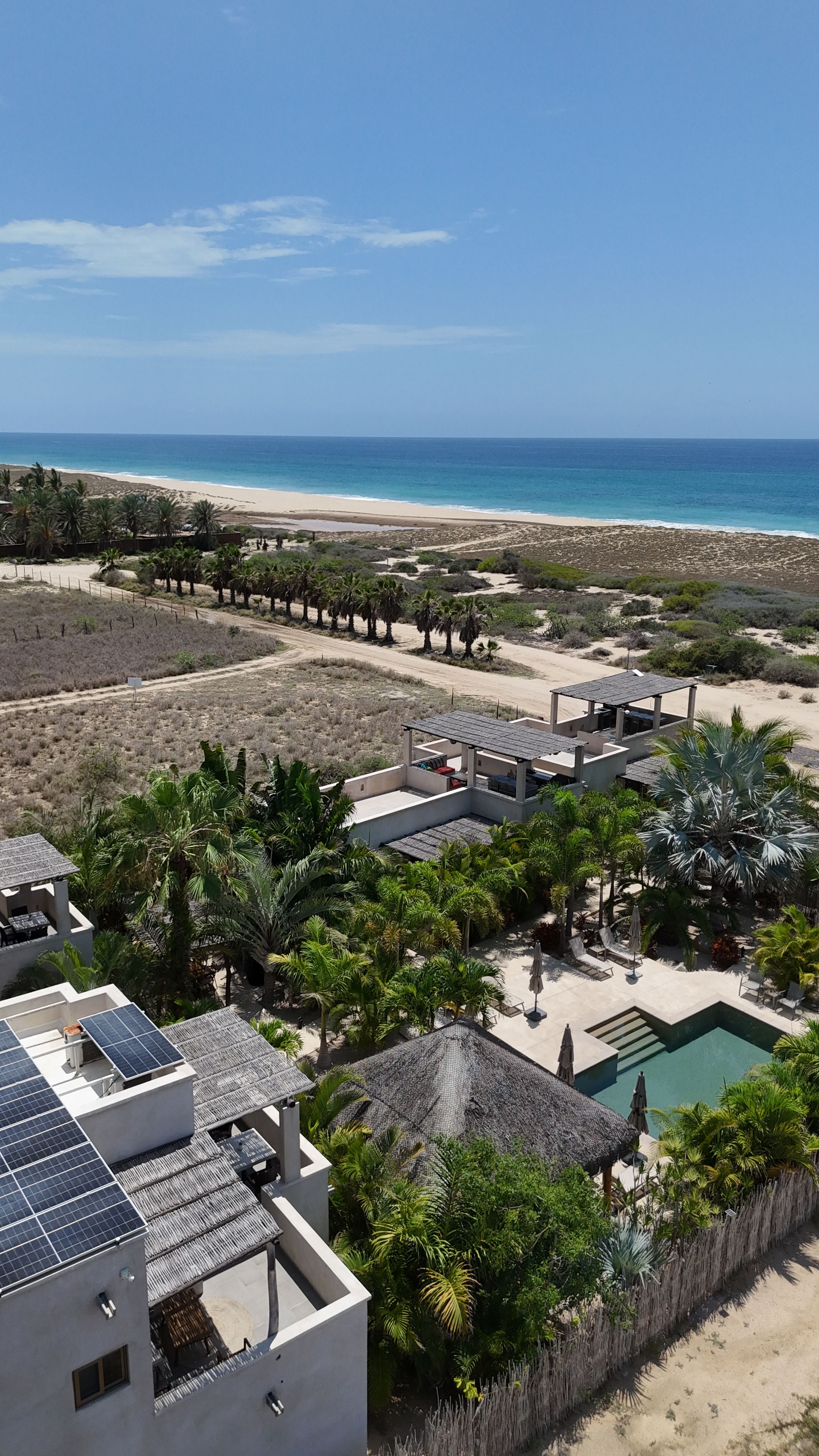 A resort with a pool, solar panels, and a view of the beach.