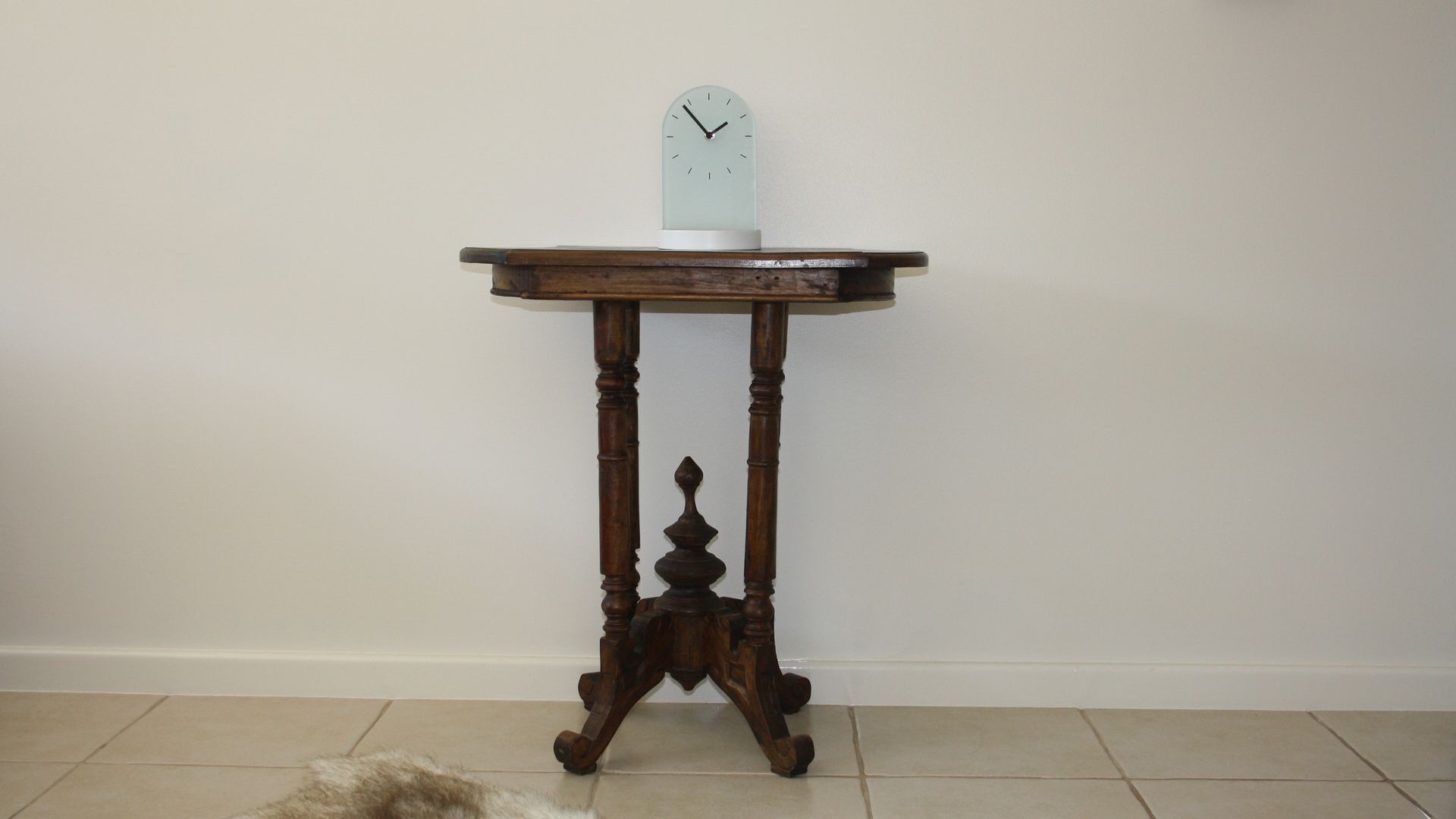A wooden table with a clock on top, positioned against a plain wall.
