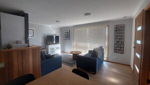 Un soggiorno moderno con televisore, divani, tavolino da caffè e zona pranzo con tavolo in legno.