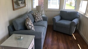 Ein Wohnzimmer mit grauem Sofa, grauem Sessel, einem Glastisch und einem Bild an der Wand.