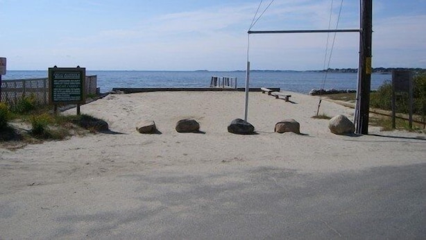 Ein Zugang zum Strand mit einem Schild, einem Weg und Blick aufs Meer.