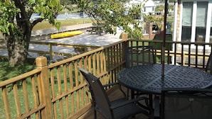Eine Holzterrasse mit einem runden Metalltisch und Stühlen, einem Picknicktisch und einem Backofen aus Ziegeln.