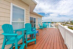 A wooden deck with turquoise Adirondack chairs, a glass door, and a view of the ocean. - Finally Beachin' - Great 4 BR Home - Ocean View & Easy Beach Access!! (Topsail Beach)