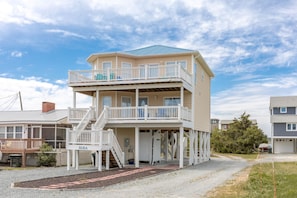 A two-story building with a balcony on the upper level, a covered area with stairs, and a garage in the background. - Finally Beachin' - Great 4 BR Home - Ocean View & Easy Beach Access!! (Topsail Beach)