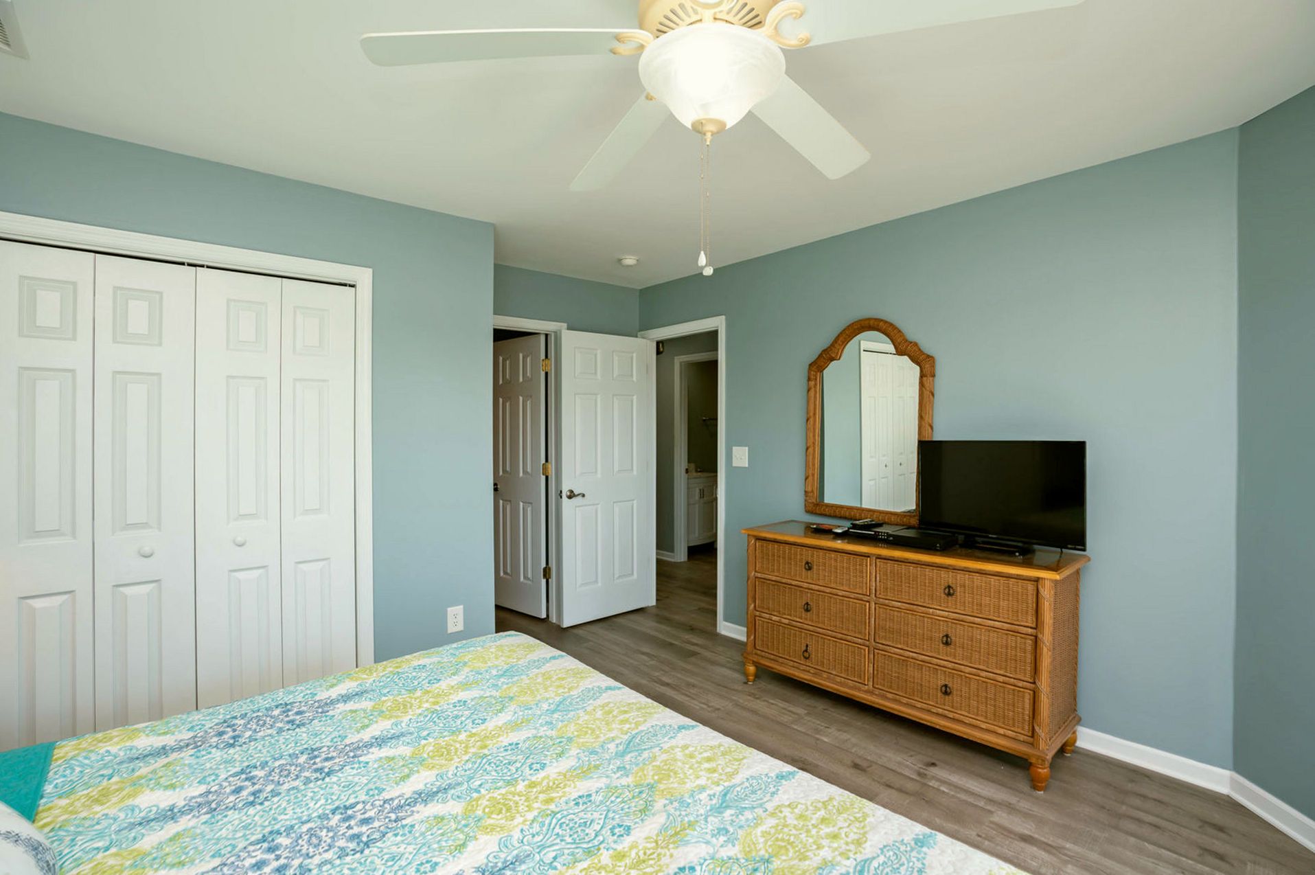 Un dormitorio con cama, cómoda, televisor y ventilador de techo.