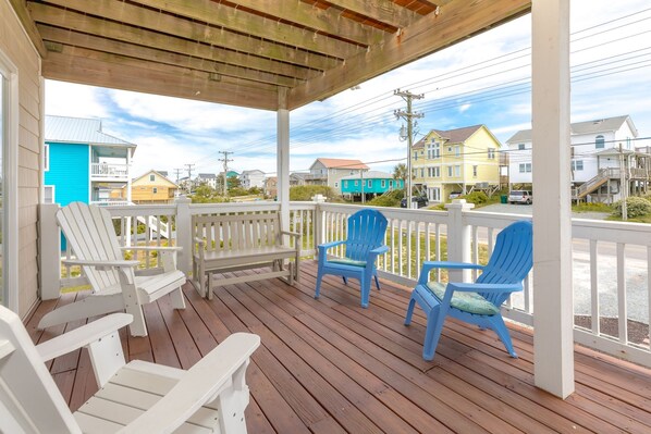 A wooden deck with white and blue Adirondack chairs, a white bench, and a view of colorful houses in the background. - Finally Beachin' - Great 4 BR Home - Ocean View & Easy Beach Access!! (Topsail Beach)