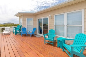 A wooden deck with turquoise Adirondack chairs and a white chair, a sliding glass door, and a white railing. - Finally Beachin' - Great 4 BR Home - Ocean View & Easy Beach Access!! (Topsail Beach)