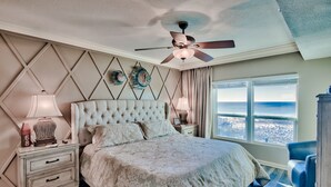 A bedroom with a large bed, a ceiling fan, a nightstand with a lamp, and a view of the beach. - Gulf Front Sea Oats 303 with Rocker Recliner, Comfy beds and Beach Service!  (Fort Walton Beach)