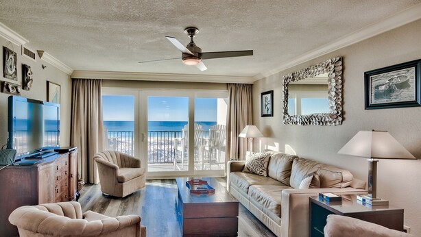 A spacious living room with a large window offering a view of the ocean, a ceiling fan, and a modern fireplace. - Gulf Front Sea Oats 303 with Rocker Recliner, Comfy beds and Beach Service!  (Fort Walton Beach)