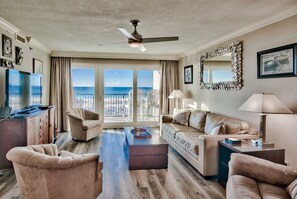 A spacious living room with a large window offering a view of the ocean, a ceiling fan, and a modern fireplace. - Gulf Front Sea Oats 303 with Rocker Recliner, Comfy beds and Beach Service!  (Fort Walton Beach)