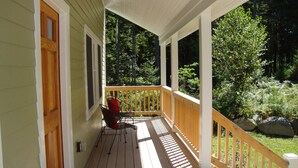 A covered porch with a wooden railing, a chair, and a door. - Gorgeous Newer Home on Mt. Desert Island, Minutes to Acadia (Bass Harbor)