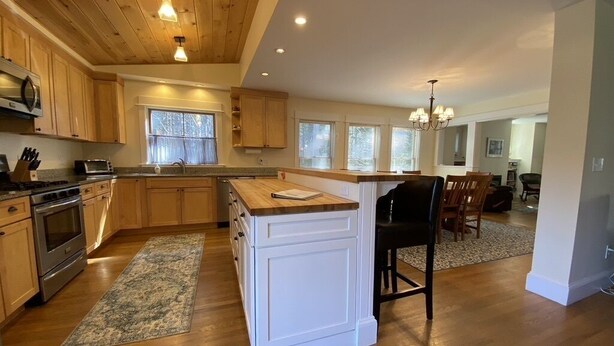 A spacious kitchen with wooden cabinets, a central island, and a dining area with a table and chairs. - Gorgeous Newer Home on Mt. Desert Island, Minutes to Acadia (Bass Harbor)