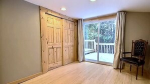 Una habitación con puerta corredera, un ventanal con cortinas, suelo de madera y una silla.