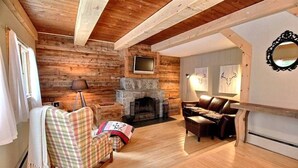 Una sala de estar acogedora con chimenea, paredes de madera, un televisor y un sofá de cuero.