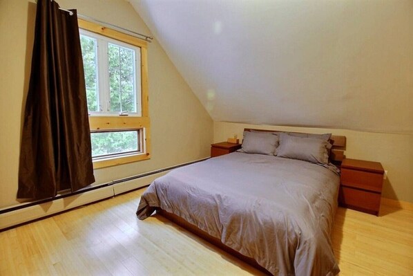 A bedroom with a single bed, a nightstand, a window with curtains, and a sloped ceiling. - Ski, Golf, Bike, Hiking, snowmobiles and more (Jay)