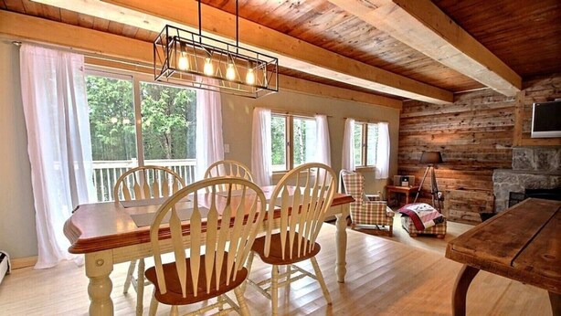 Un comedor de madera con una mesa y sillas, ventanas grandes con cortinas y una chimenea de piedra.