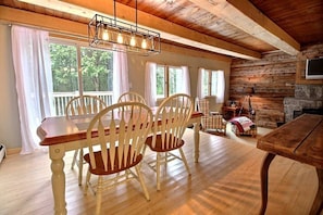 A wooden dining area with a table and chairs, large windows with curtains, and a stone fireplace. - Ski, Golf, Bike, Hiking, snowmobiles and more (Jay)