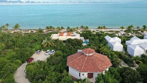 An aerial view of a coastal property with white buildings, a red-roofed house, and a clear view of the ocean.