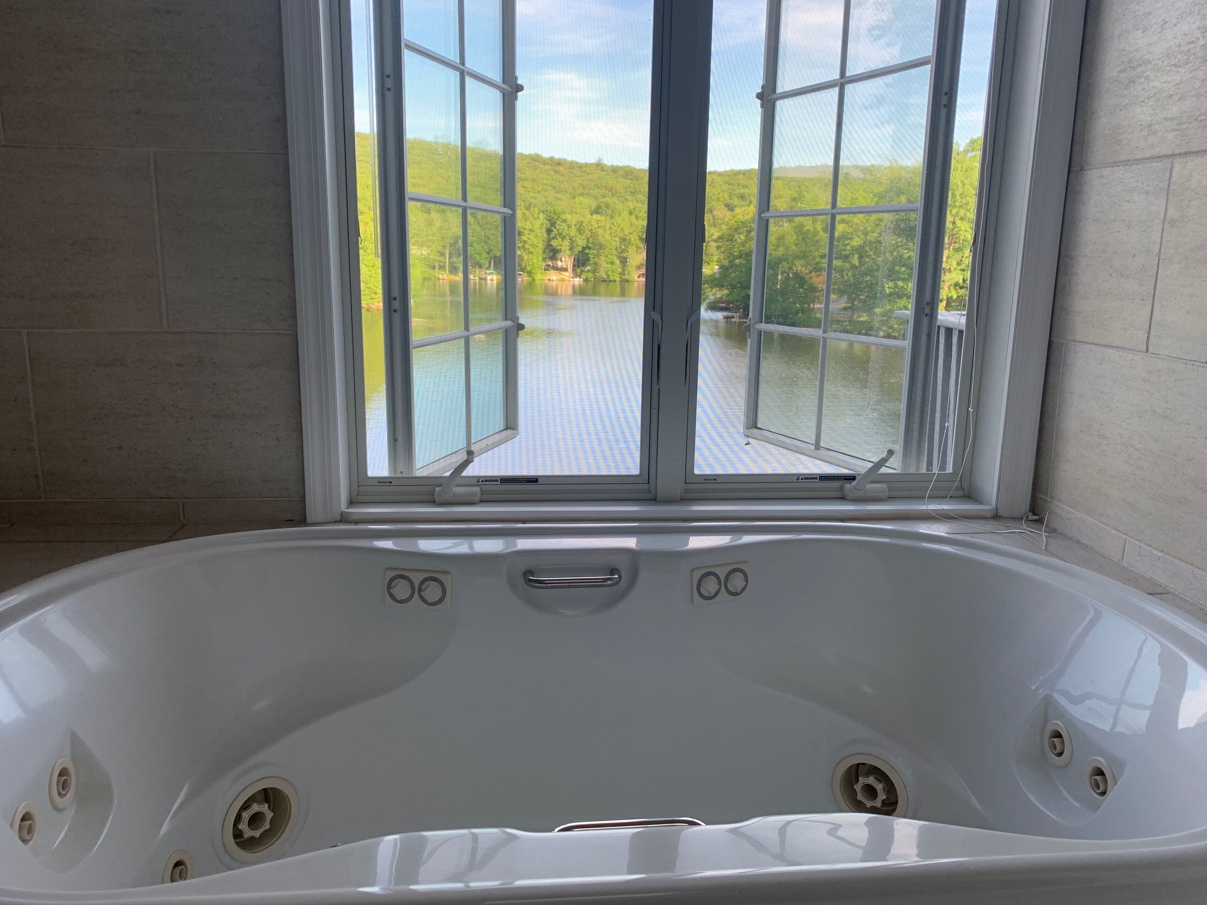 A bathroom with a large bathtub, a window with a view of a lake and trees, and tiled walls.