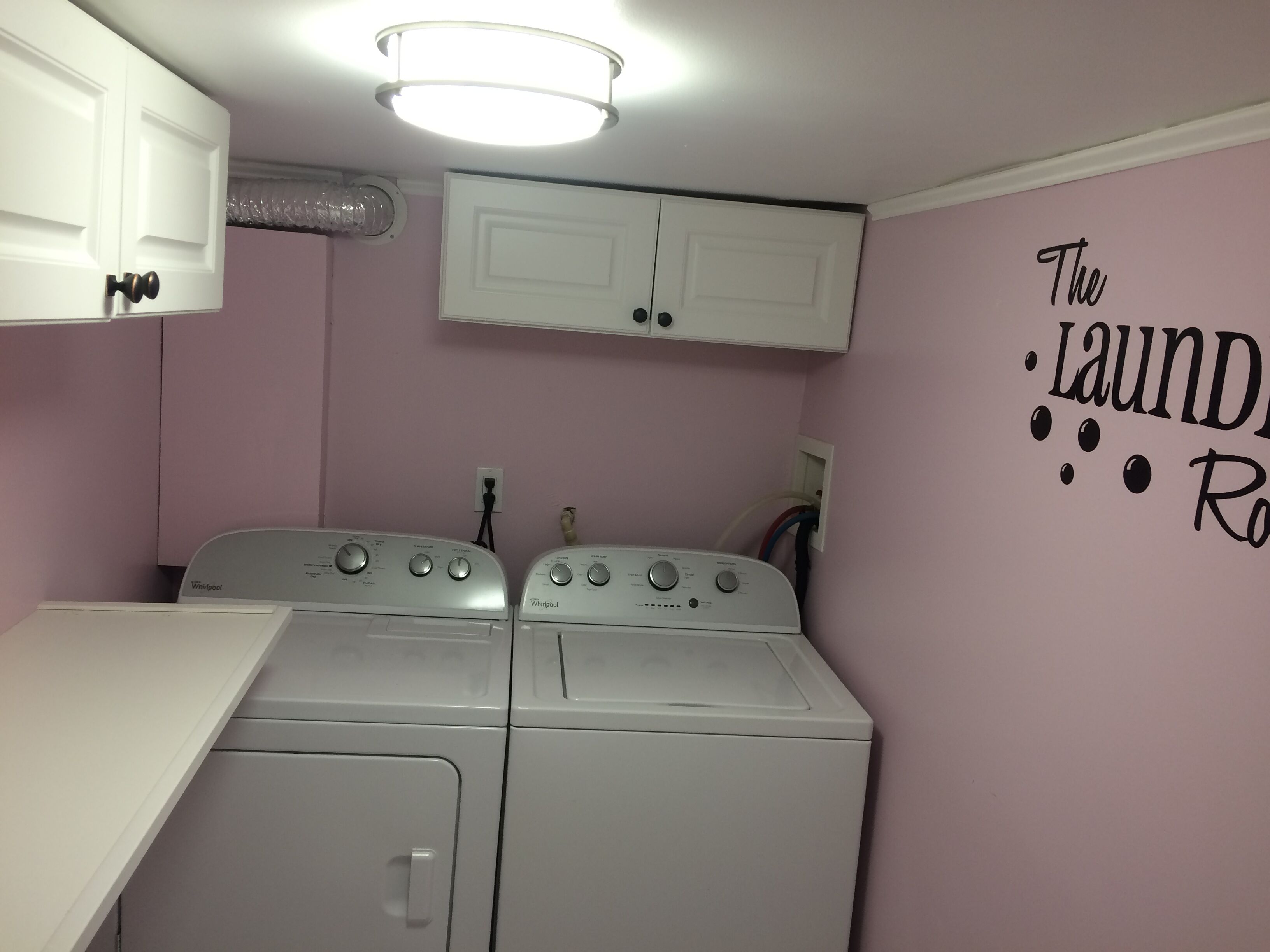 Ein Waschraum mit zwei Whirlpool Waschmaschinen, einer weißen Arbeitsplatte und einer Wand mit der Aufschrift 'The Laundry Room'.